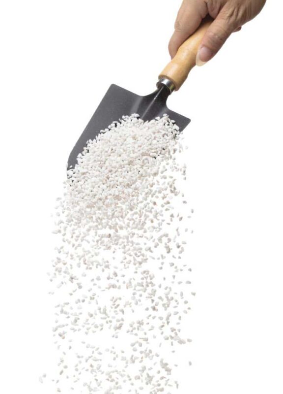 Hand holding a gardening shovel from which perlite falls